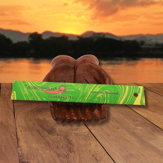 pk of auroshikha incense sitting on a carved wooden hand on a jetty, in front of a golden sunset