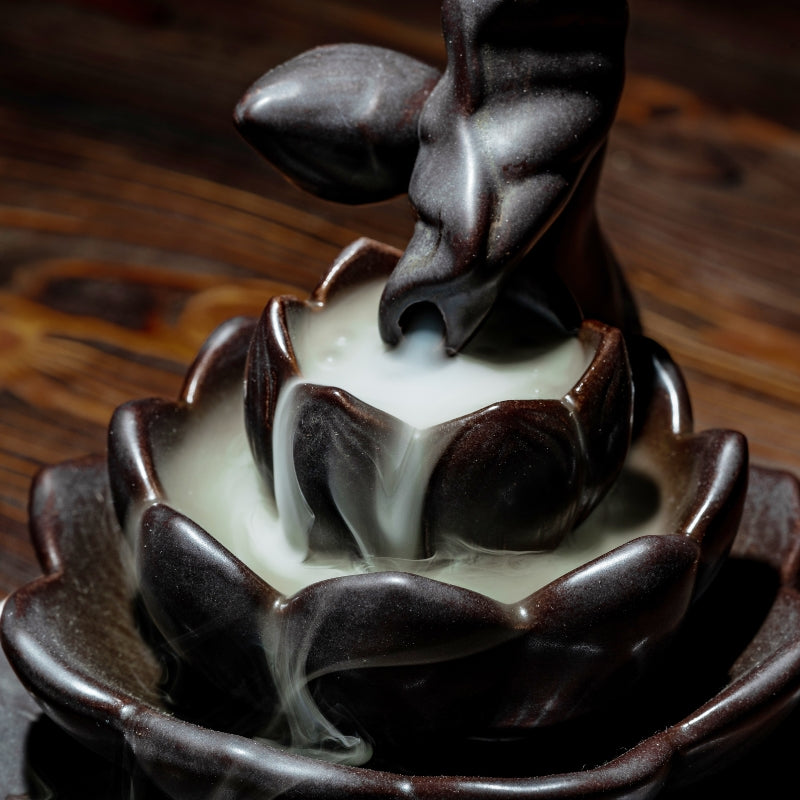 ceramic backflow lotus incense burner with smoke billowing out of the stem,  on a wooden table