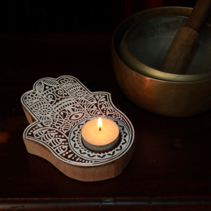 lit beeswax tea light candle in a hamsa hand tealight holder next to brass singing bowls