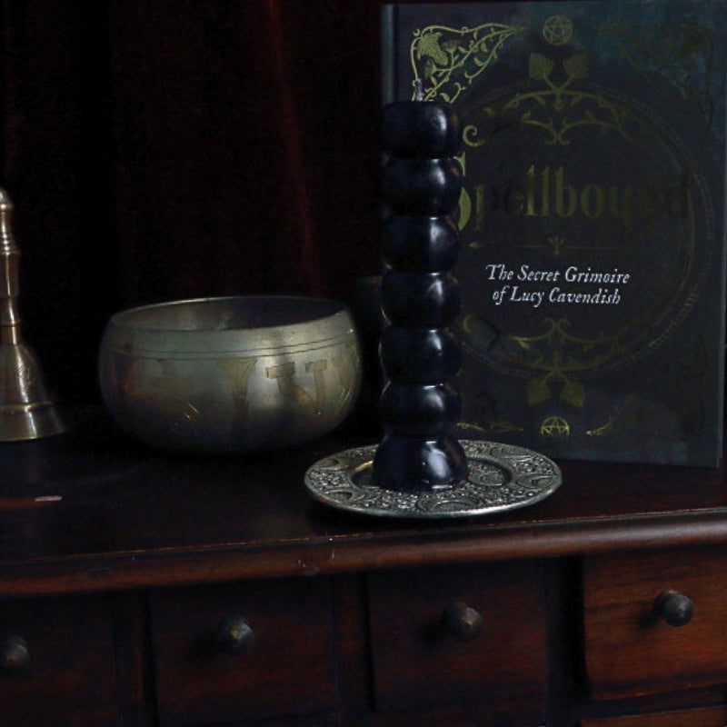 black 7 knob candle in front of a singing bowl and spellbound grimoire
