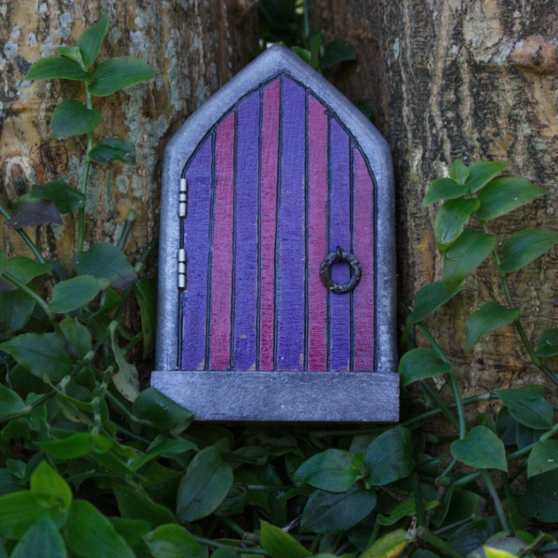 purple and pink handmade fairy door, sitting against a tree