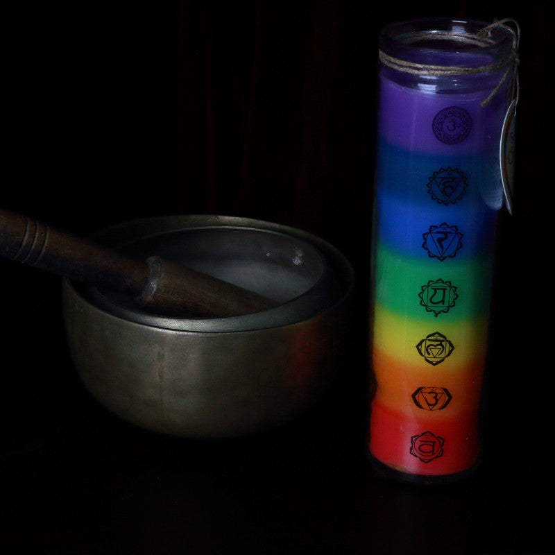 chakra candle next to a brass singing bowl