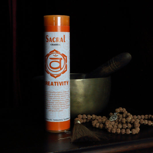Orange sacral chakra pillar candle in front of a singing bowl with mala beads