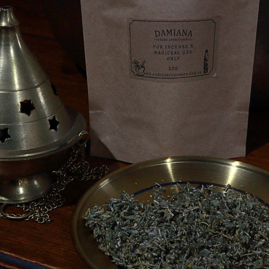 Incense burner, bag labeled 'Damiana', and a bowl of dried herbs on a wooden surface.