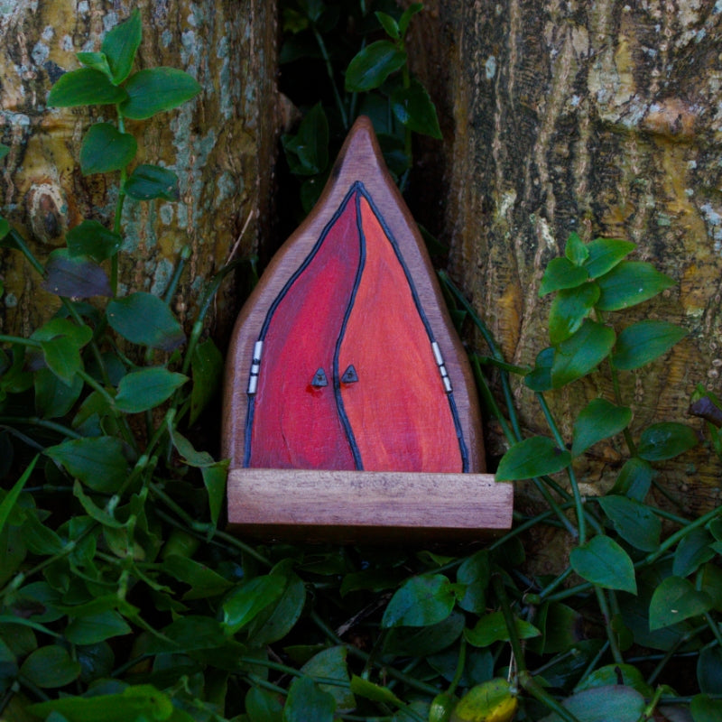 fairy door made of wood with orange and red flames as doors, nestled between two trees in a bed of greenery