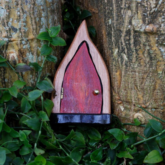 fairy door made from wood with a red flame painted on the front, sitting in front of a tree