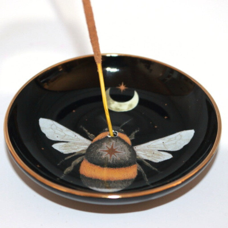 black incense dish with a bee and crescent moon. Stick of incense in the centre hole.