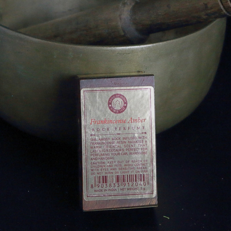 label on the back of a rosewood rock perfume box, standing in front of a brass singing bowl