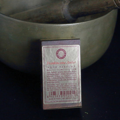 label on the back of a rosewood rock perfume box, standing in front of a brass singing bowl