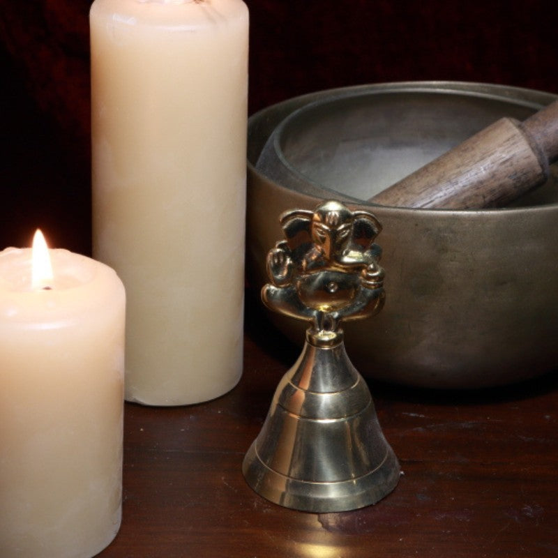 brass bell with ganesh on handle next to beeswax candles and singing bowls