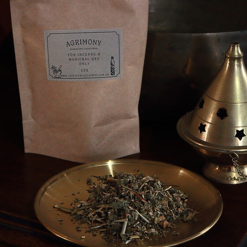 Bag of Agrimony incense with a brass dish and cone incense burner on a dark surface