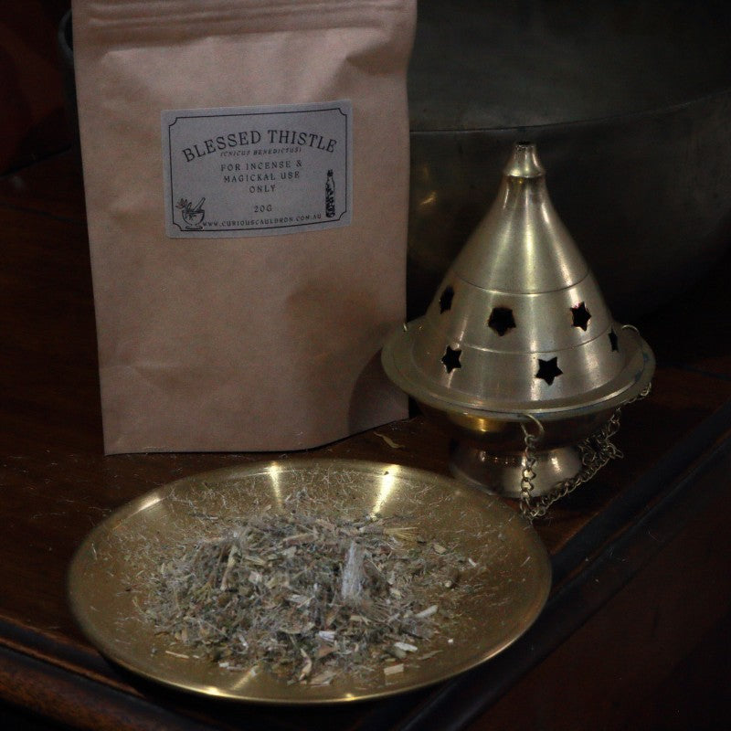 Blessed Thistle incense on a brass plate with a cone incense burner and packaging.