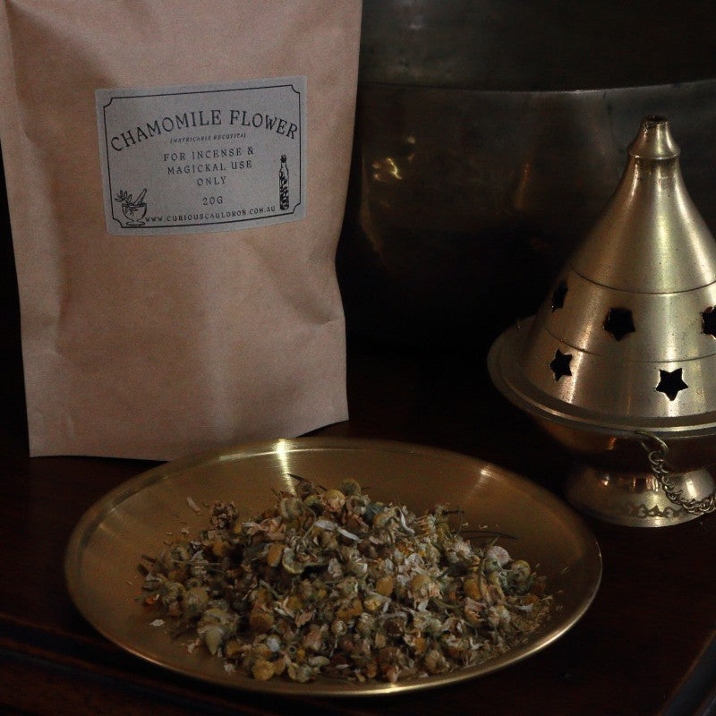 Chamomile flower package, bowl of chamomile flowers, and brass incense burner on a dark surface.