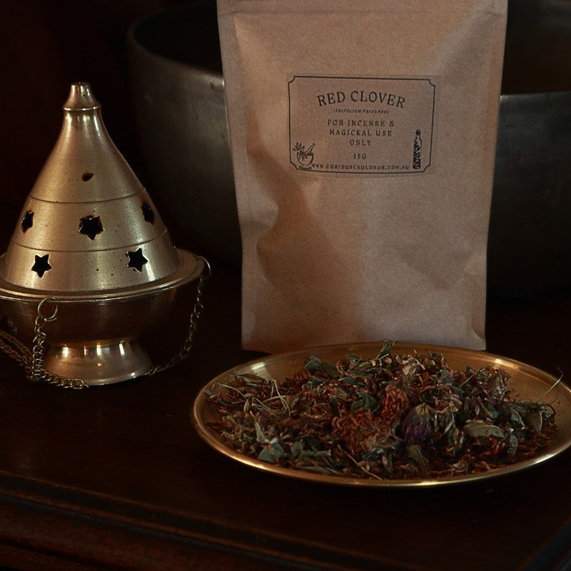 Incense burner, bag of red clover, and plate of dried red clover on a dark surface