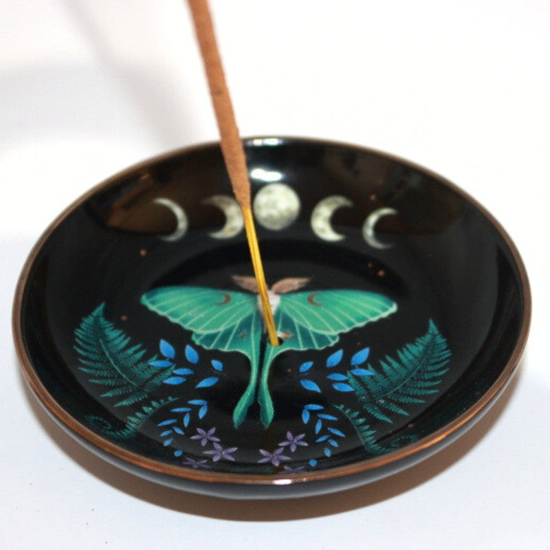 black incense dish with a luna moth and ferns under a picture of the moon phases. stick incense in the centre hole of the dish