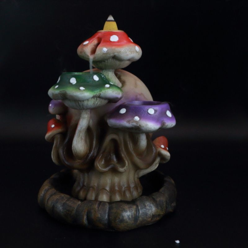 backflow incense cone burner of a skull with colourful mushrooms growing out the side of it, with incense smoke flowing down the mushrooms.