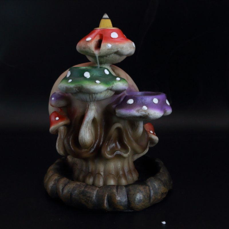 backflow incense cone burner of a skull with colourful mushrooms growing out the side of it, with incense smoke flowing down the mushrooms.