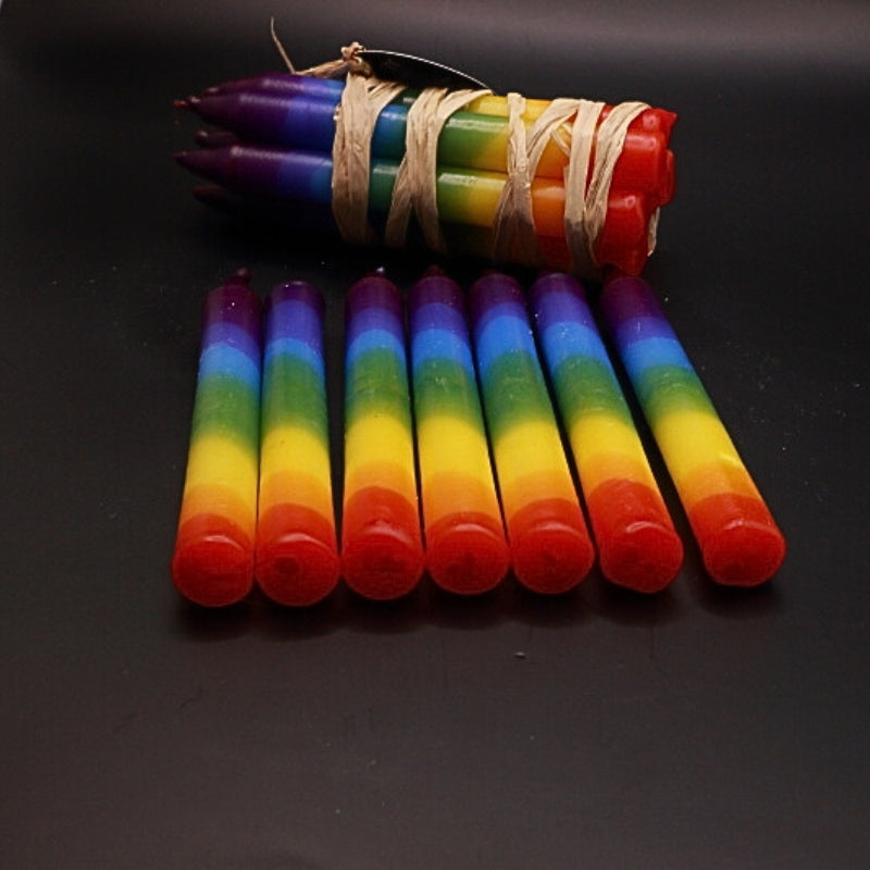 rainbow coloured candles laid out in a row of 7 in front of a bundle of rainbow candles tied with raffia