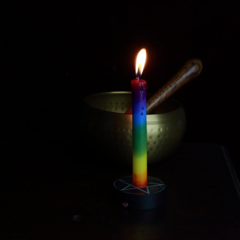 rainbow spell candle in a pentacle candle holder in front of a brass singing bowl