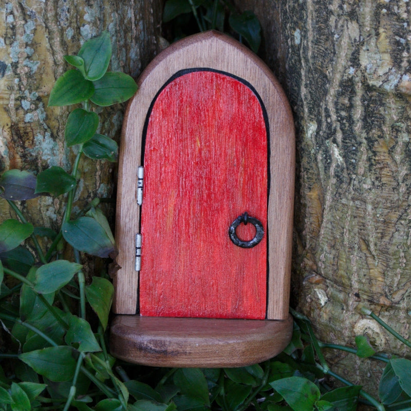 Wooden fairy door with a red door, standing in front of a tree