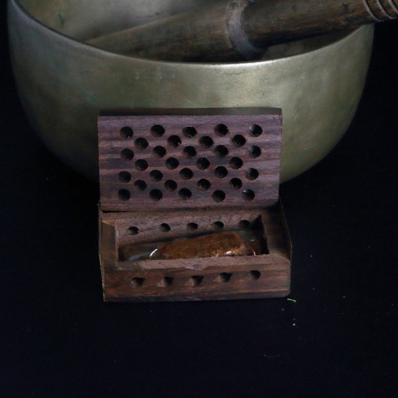 open rosewood cutwork box containing myrrh resin standing in front of a brass singing bowl