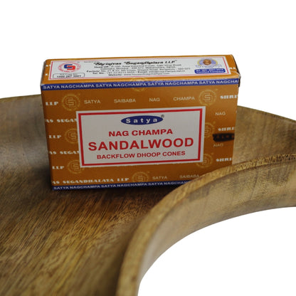 light brown box of incense cones with blue borders and a white label on the front  with a red border, blue and white ellipse Satya trademark logo on the front with product name written in red sitting on a wooden crescent moon shaped dish