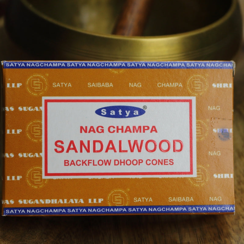 brown box of satya backflow incense cones sitting on a wooden table in front of a brass singing bowl with wooden striker