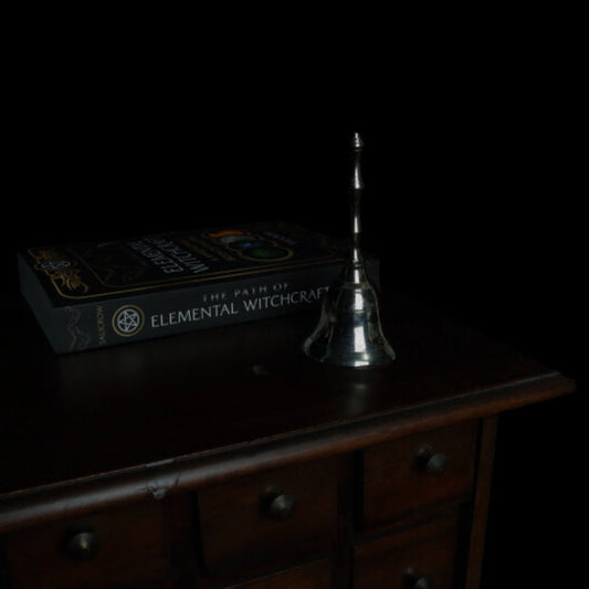 silver altar bell in front of a witchcraft book, on an apothecary cabinet