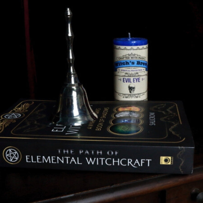 silver altar bell  on a witchcraft book in front of a candle