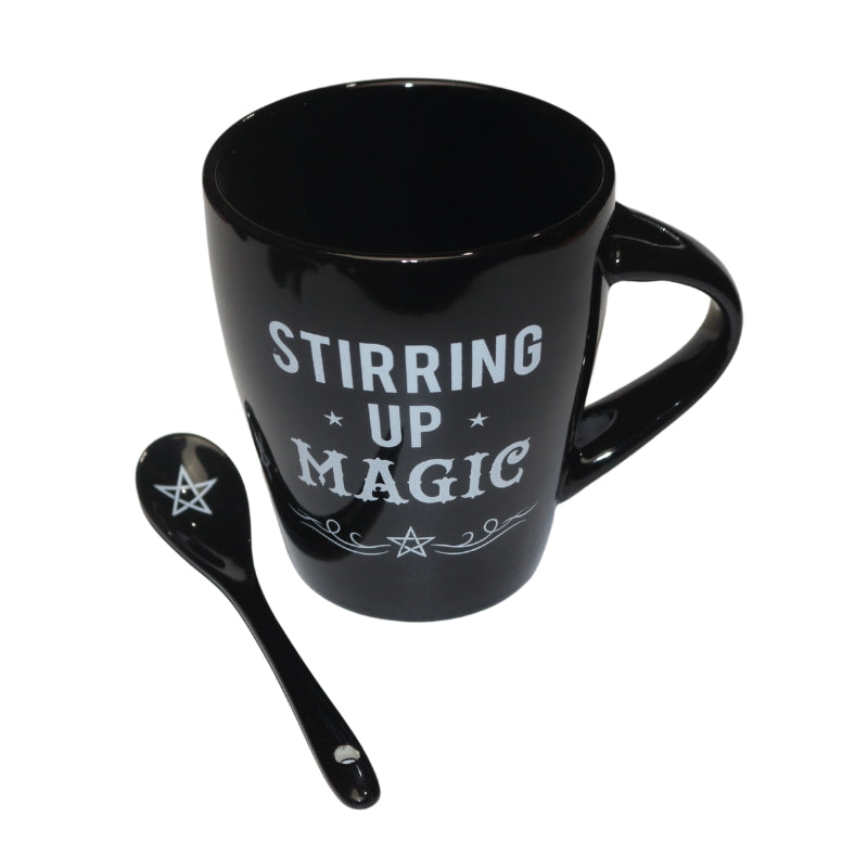 black mug decorated with the words "stirring up magic "  written in white, and black spoon decorated with a white pentacle.