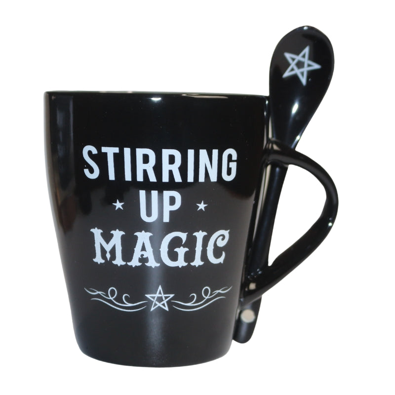 black mug decorated with the words "stirring up magic "  written in white, and black spoon decorated with a white pentacle.