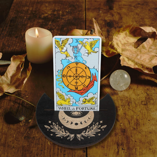 Wheel of fortune tarot card in a black tarot card holder on a wooden table in front of autumn leaves, an apple, crystal ball and white pillar candle
