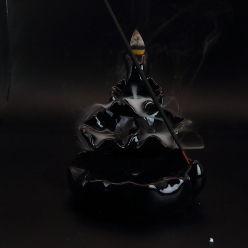 Ceramic Waterfall Backflow Incense Cone Burner with a sitck incense in front and smoke billowing down the front on a black background