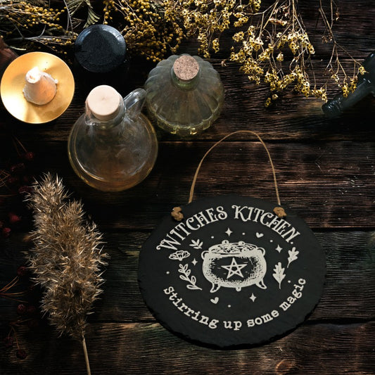 kitchen witch sign on a wooden table with herbs and jars of oil