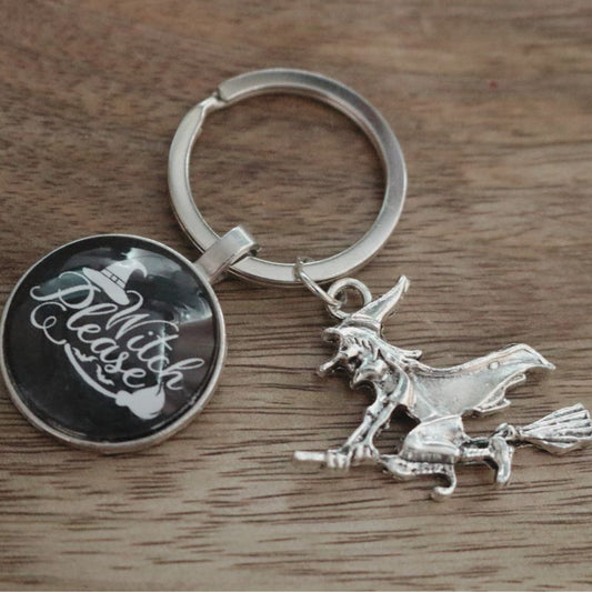 keyring of a witch riding a broomstick, with a black circle attached to it saying "witch please" in white writing