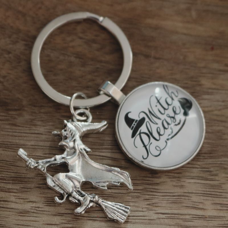 key ring with a silver witch riding a broomstick, a circle attached to the keyring that reads "witch please"