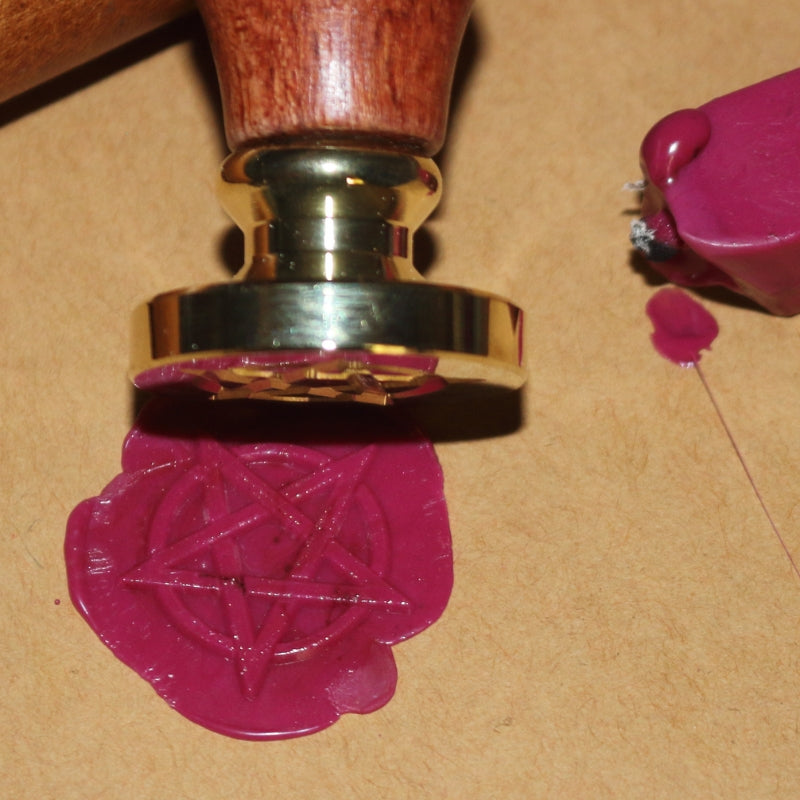 pentagram wax seal in pink on brown paper with the wax seal stamp and sealing wax next to it