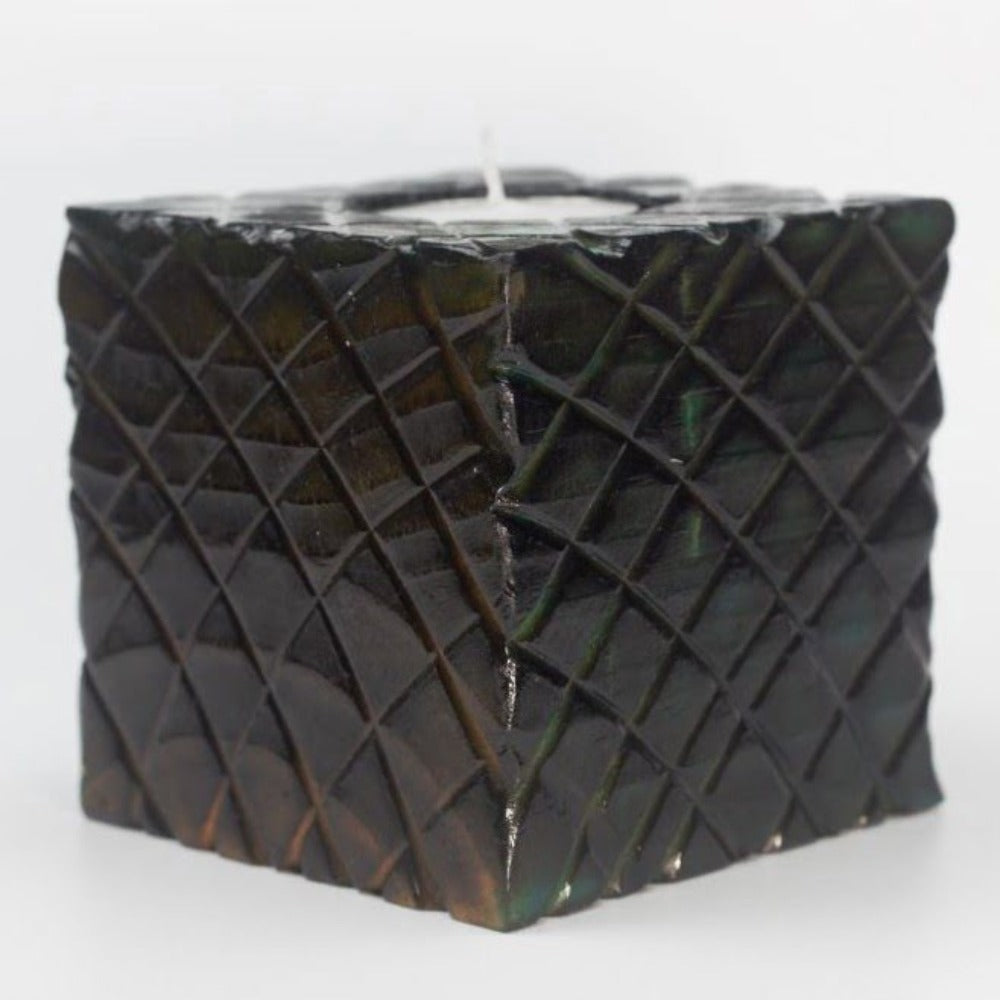 yellow and green sides of multi coloured wooden square candle holder with diagonal lines etched to resemble dragon scales. Containing a white tea light candle, on a white background