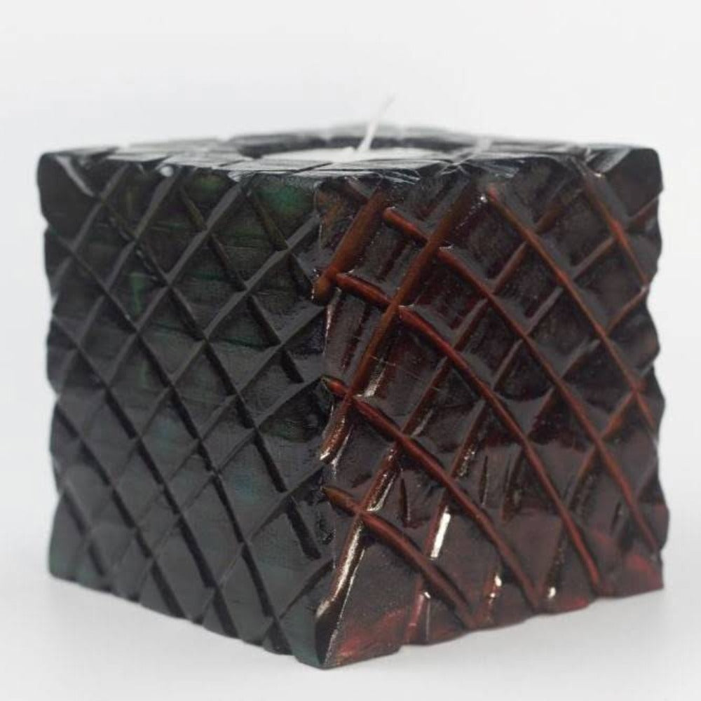 green and red sides of multicoloured wooden square candle holder with diagonal lines etched to resemble dragon scales. Containing a white tea light candle, on a white background