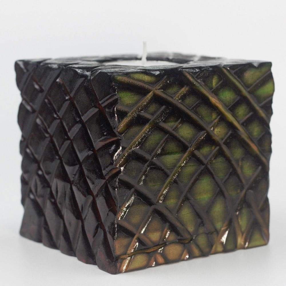 green and red sides of multicoloured  wooden square candle holder with diagonal lines etched to resemble dragon scales. Containing a white tea light candle, on a white background