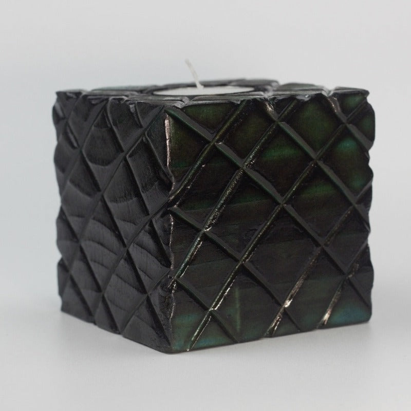 green wooden square candle holder with diagonal lines etched to resemble dragon scales. Containing a white tea light candle, on a white background