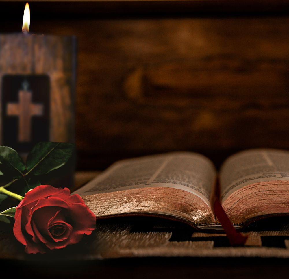 cross wooden tealight candle holder  solid hardwood with white tea light in top behind a red rose and an old book, in front of a wooden background 
