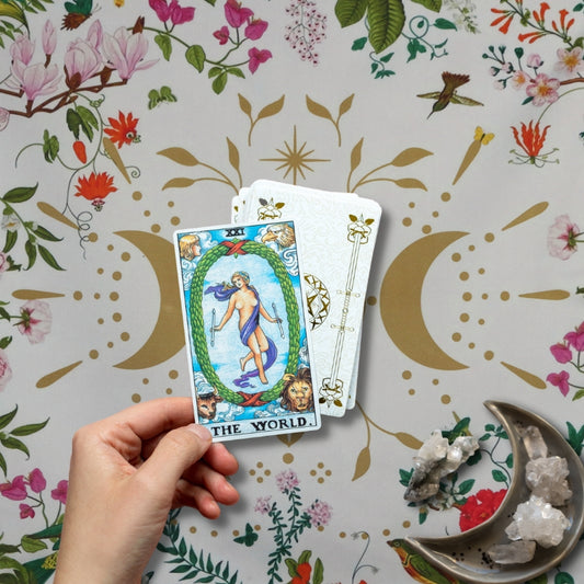 Tarot practitioner laying tarot cards onto a white tarot cloth with floral borders embellished with a gold moon in between two gold crescent moons