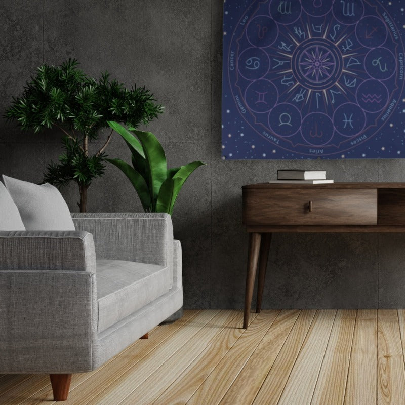 blue astrology tarot cloth/ wall hanging hung on grey tiled wall, above brown side table , next to a grey armchair and  two pot plants with green foliage plants in them 