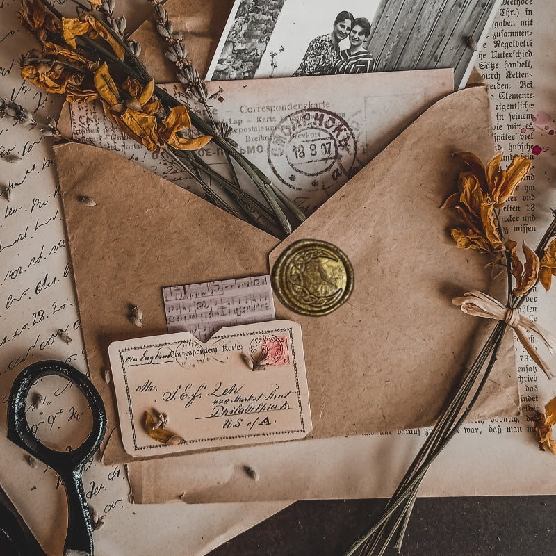 old envelope, sealed with a gold celtic crescent moon design wax seal, sitting atop vintage style papers and photographs with dried flowers