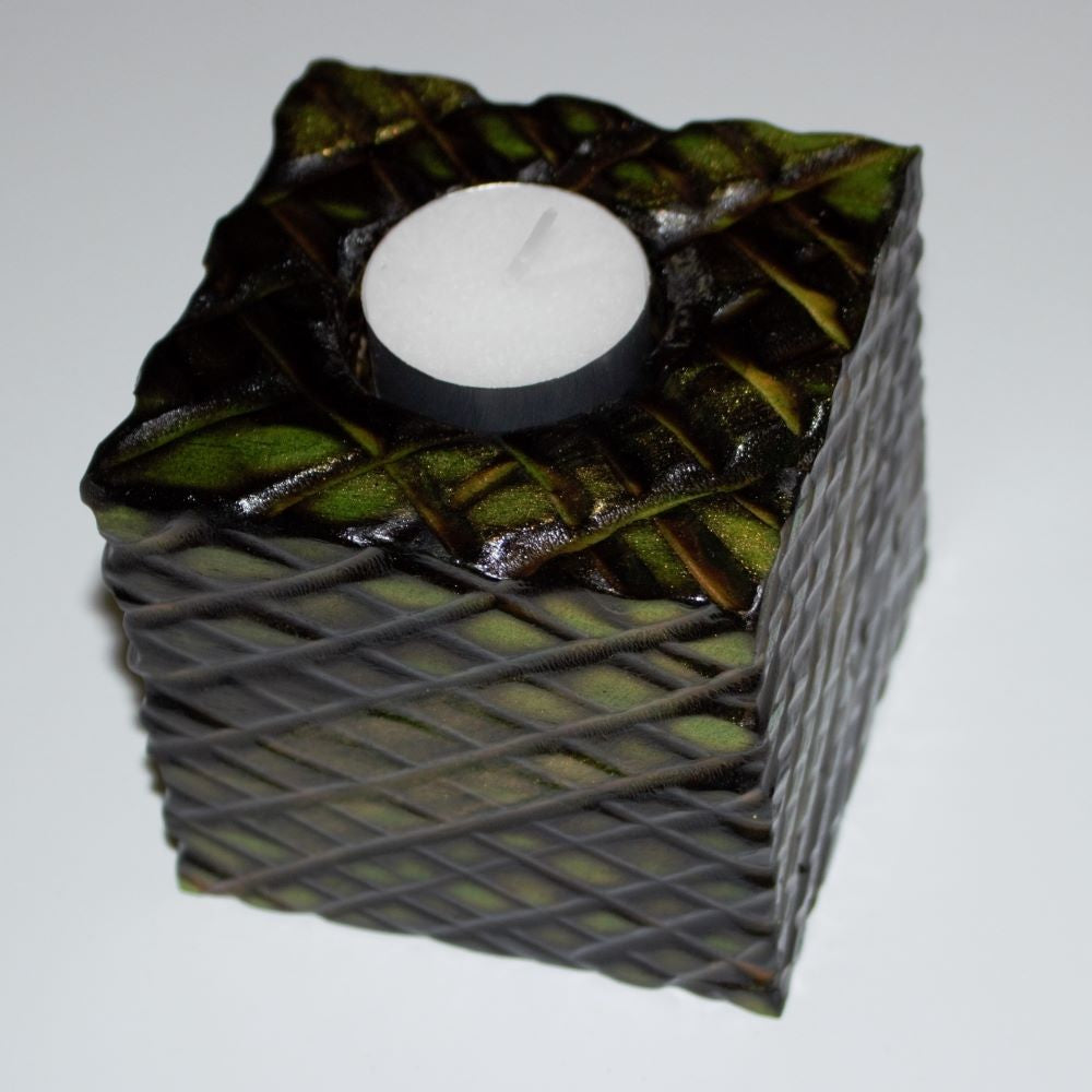 green and gold wooden square candle holder with diagonal lines etched to resemble dragon scales. Containing a white tea light candle, on a white background