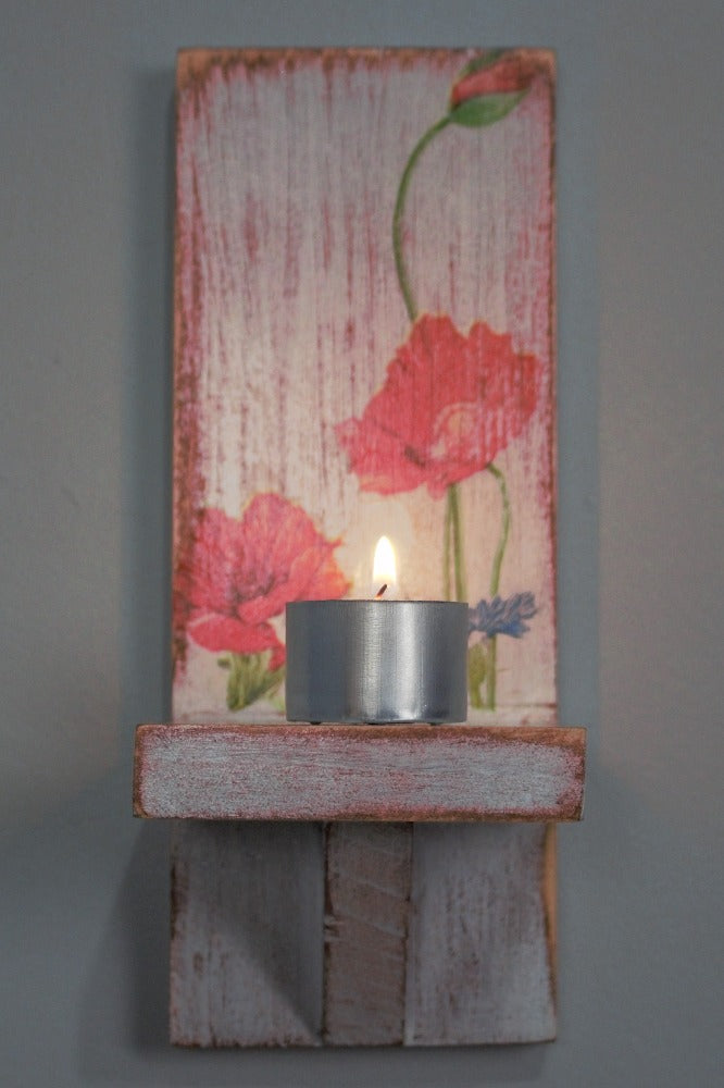 9 hour metal tealight candle sitting on a red and white wooden wall mounted candle or ornament  shelf decorated with red and blue flowers 