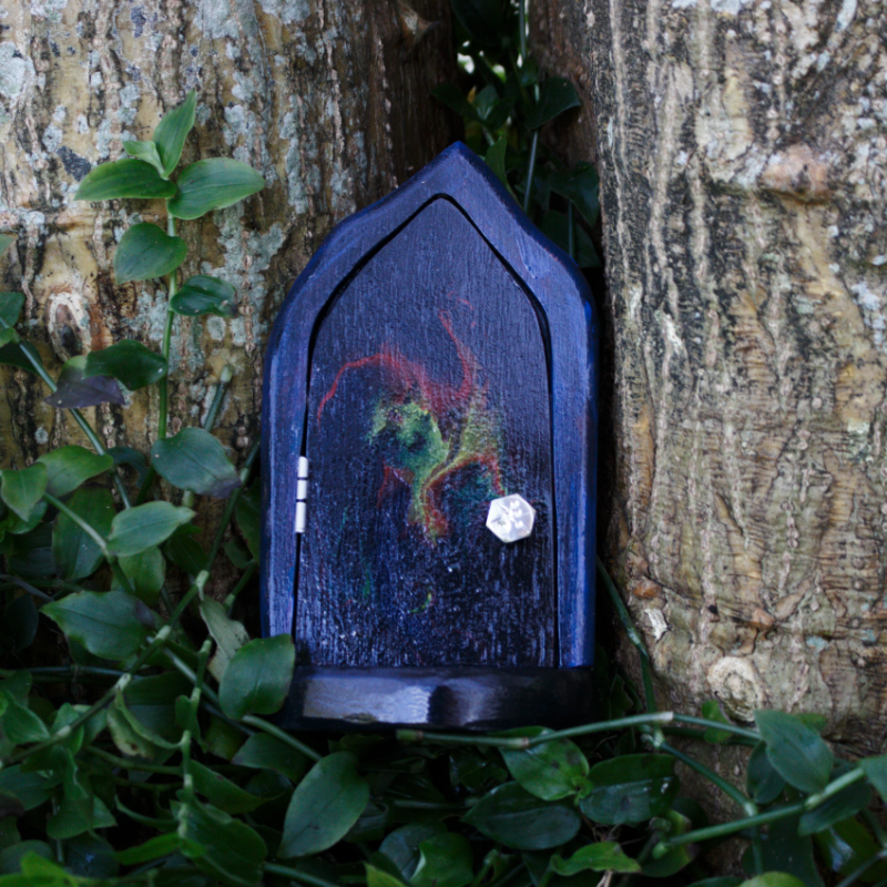 black fairy door with a galaxy painted on the front, sitting in front of a tree