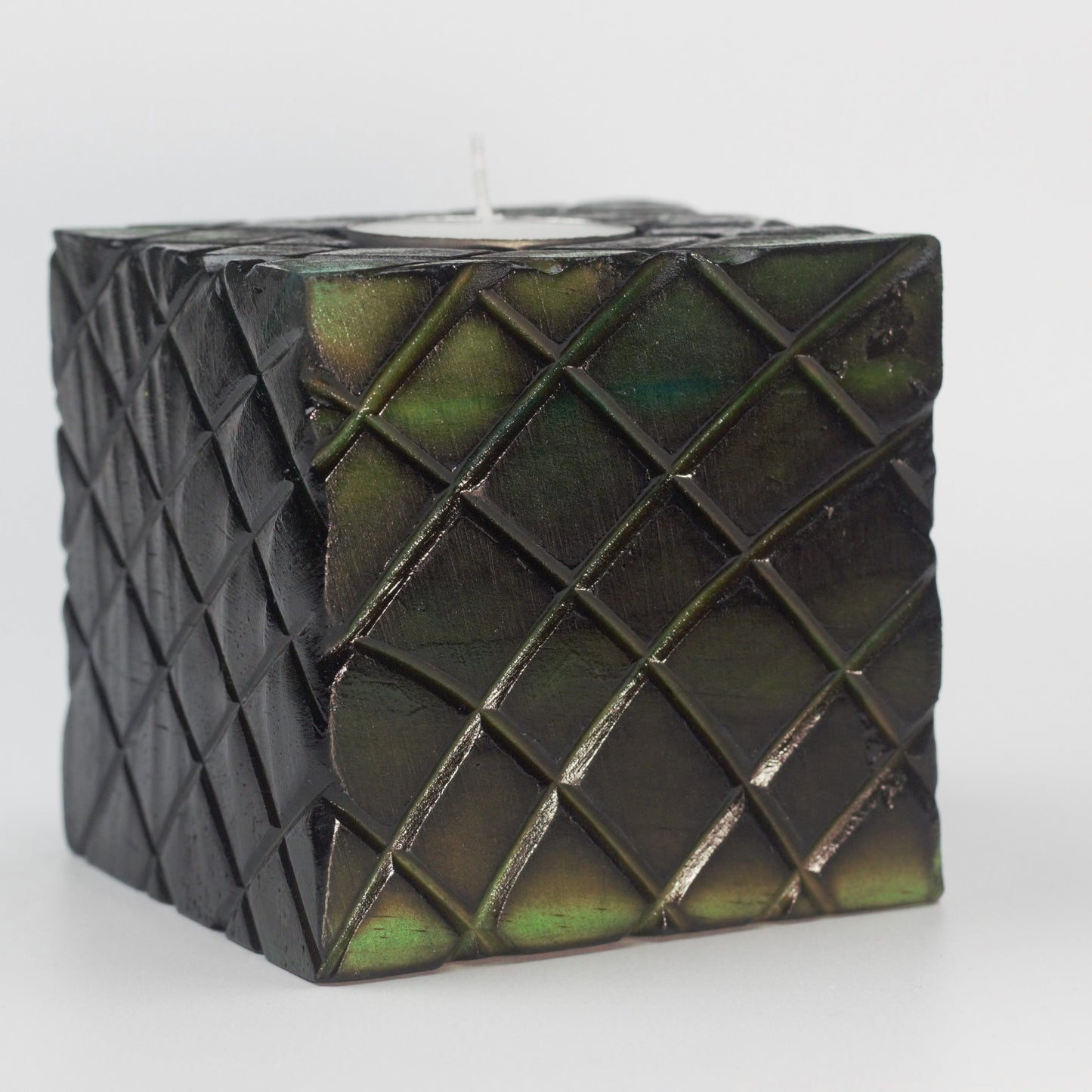 green wooden square candle holder with diagonal lines etched to resemble dragon scales. Containing a white tea light candle, on a white background