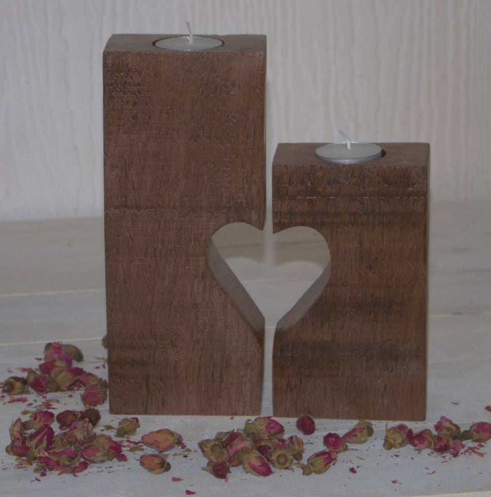 2 wooden candle holders with 1/2 heart cut in each, paired to make a heart, containing tea light candles, sitting on a white table with dried rosebuds